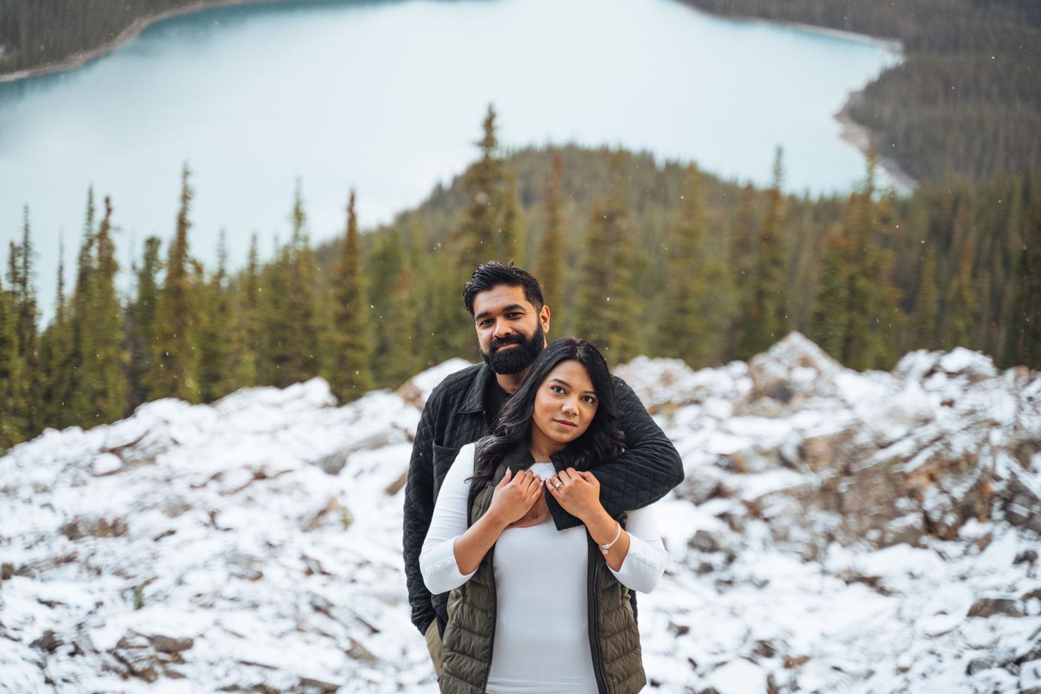 Couple embraces by a snowy lake in the Rockies. Banff winter engagement session.