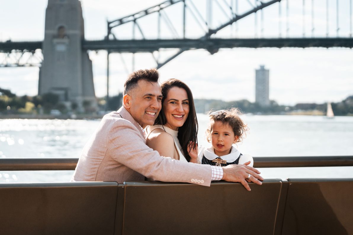 Family sitting on a bench in front of the Sydney Harbour Bridge during a family photoshoot, capturing the stunning city