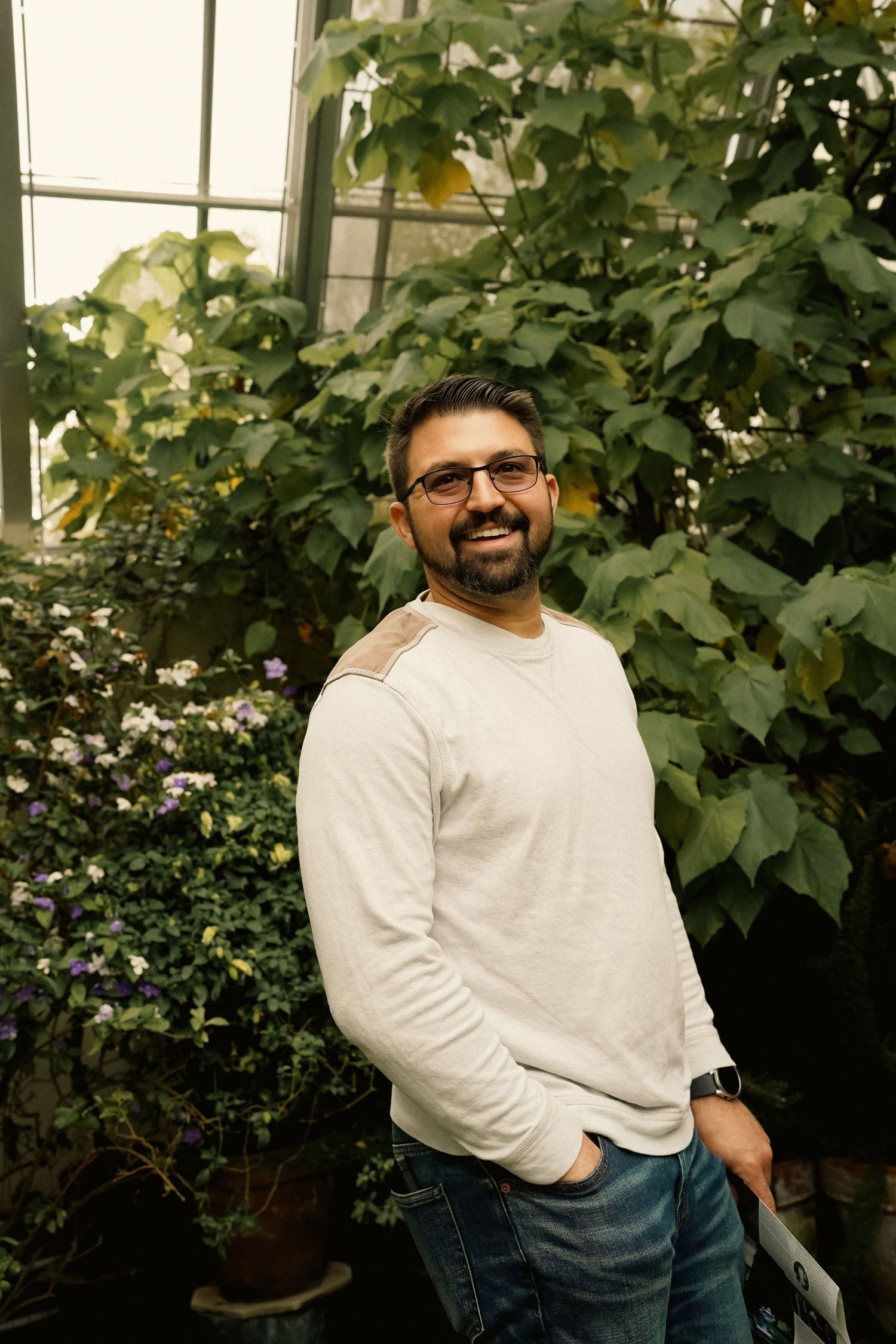 Casual portrait in greenhouse with lush green plants in background.