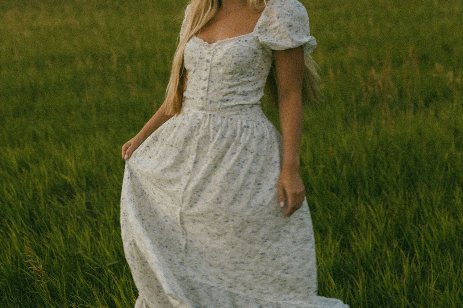 Woman in white floral midi dress with puff sleeves standing in a lush green field.