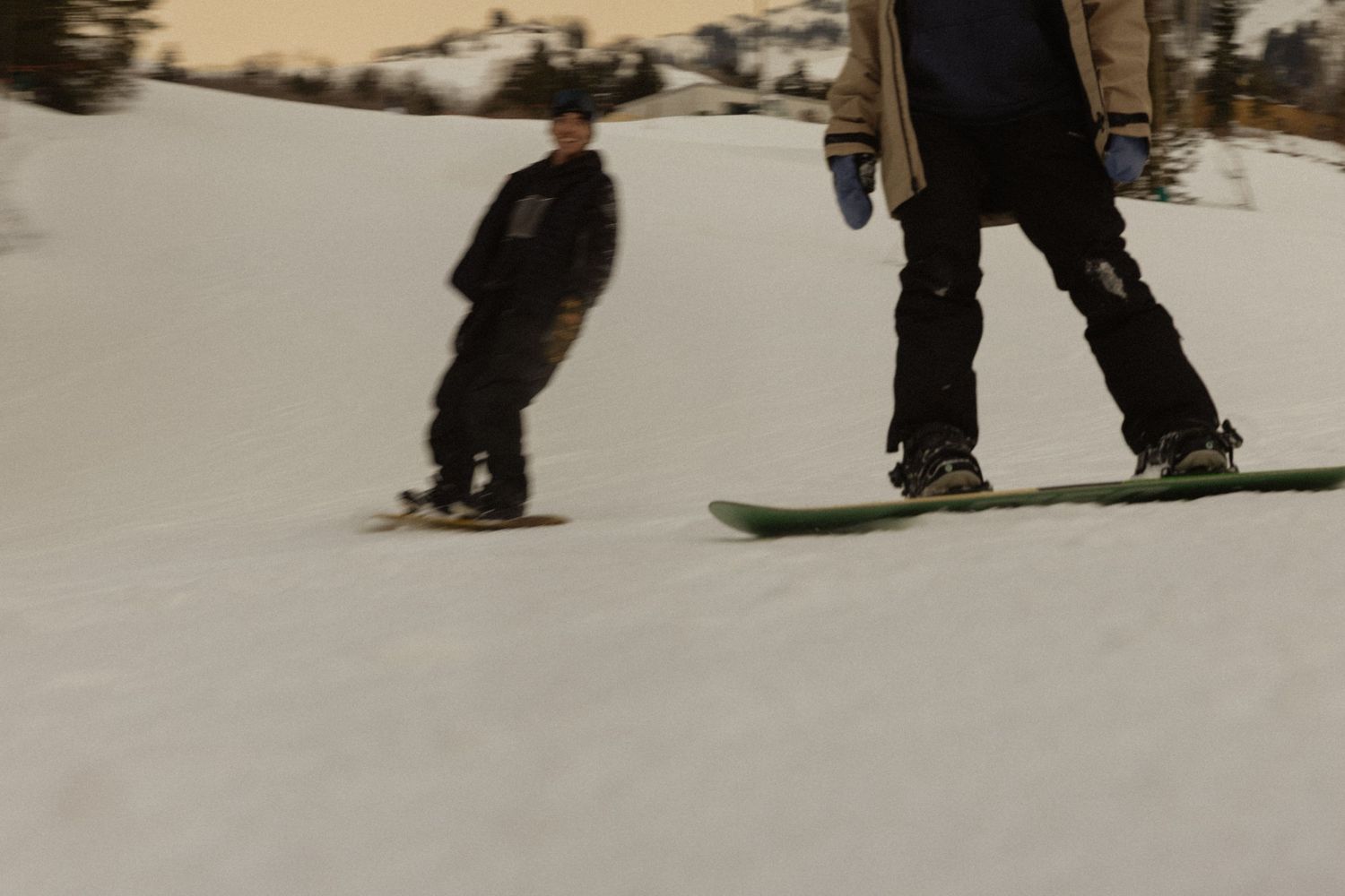 Silhouettes of snowboarders glide across a snowy slope.