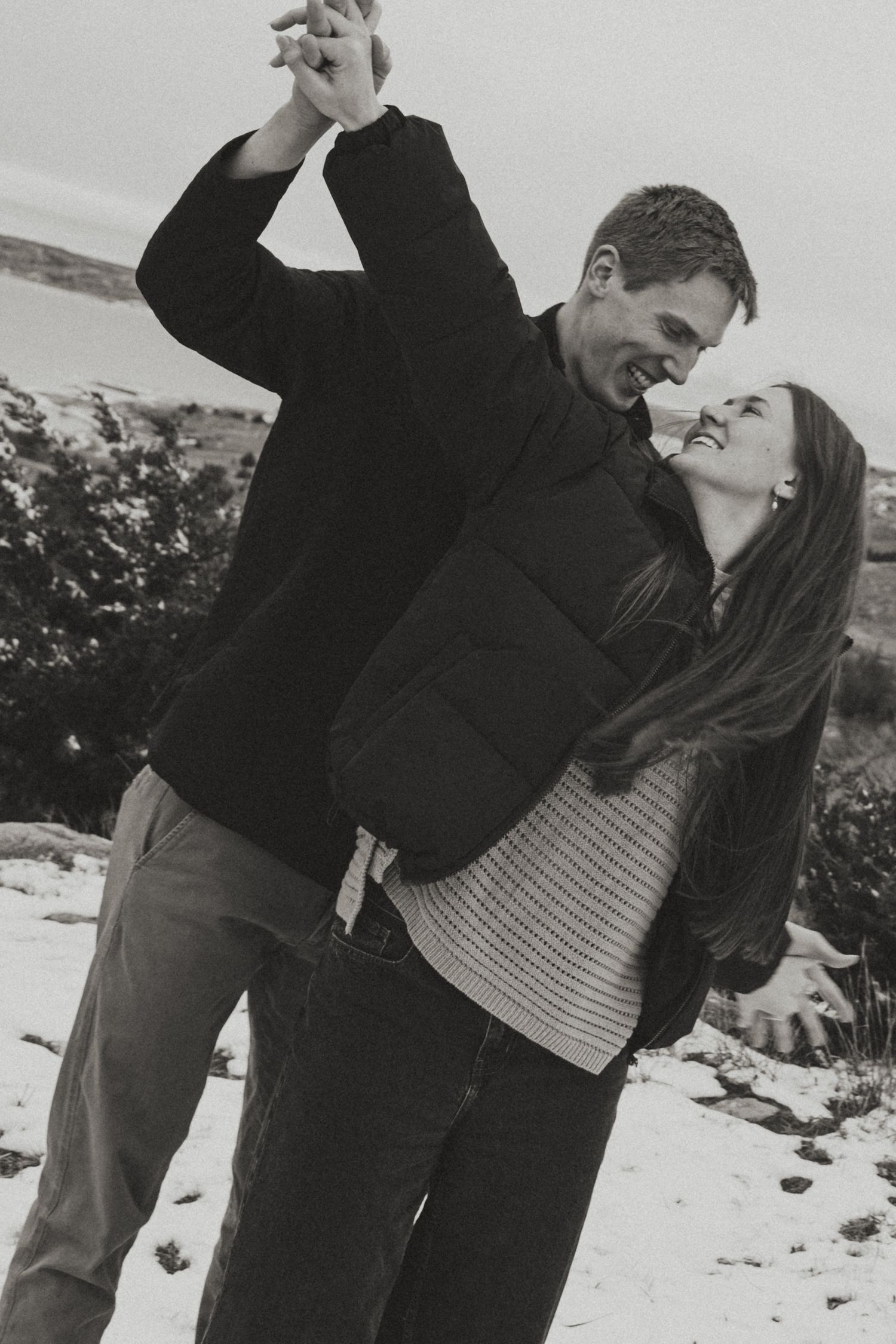 Black and white photo of a couple dancing playfully in the snow, the man spinning the woman as she laughs joyfully.