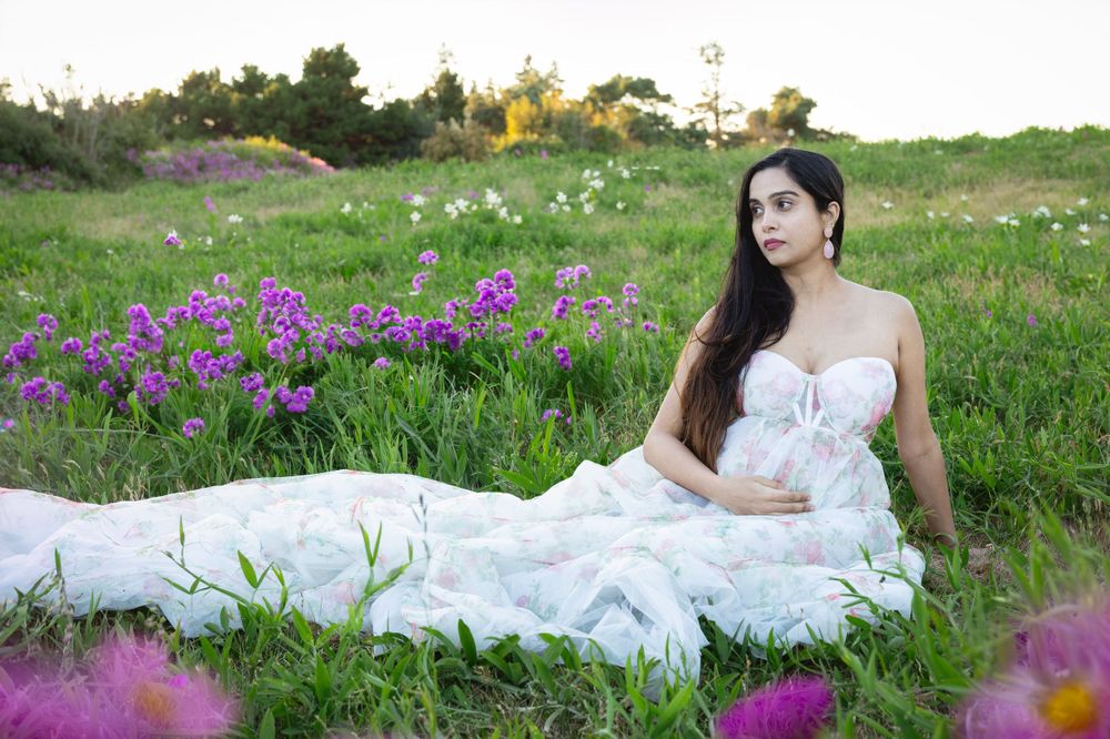 A white flowing dress contrasts beautifully against a meadow filled with vibrant purple and yellow wildflowers at sunset.