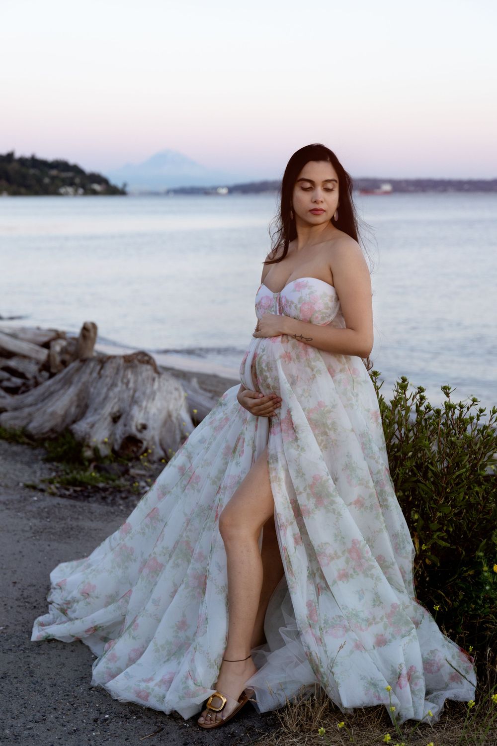 Elegant floral maternity gown photoshoot at sunset by the ocean with mountain views in the background.