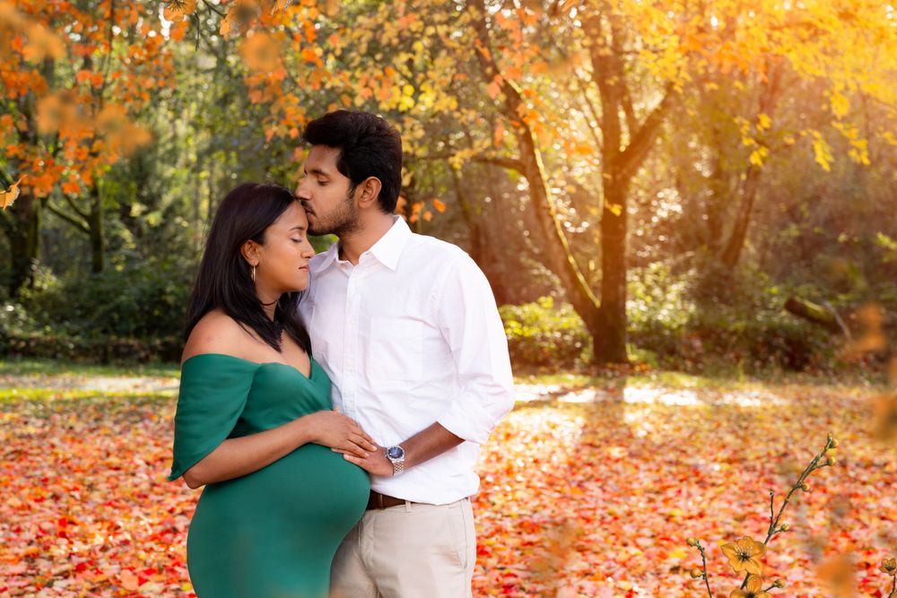 A couple shares an intimate moment in an autumn park with golden sunlight and fallen leaves on the ground.