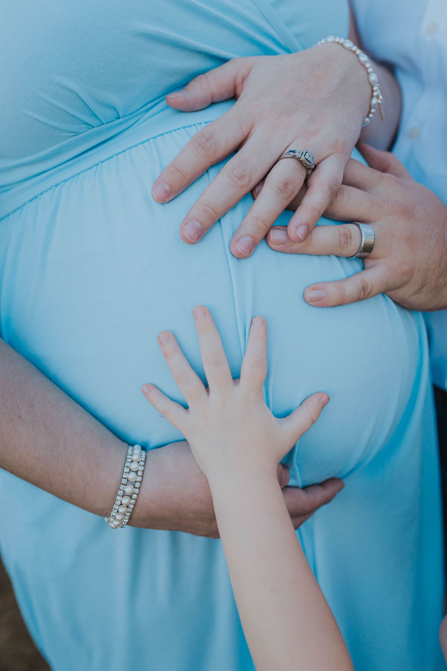 Close-up of hands cradling a pregnant belly in a teal maternity dress.