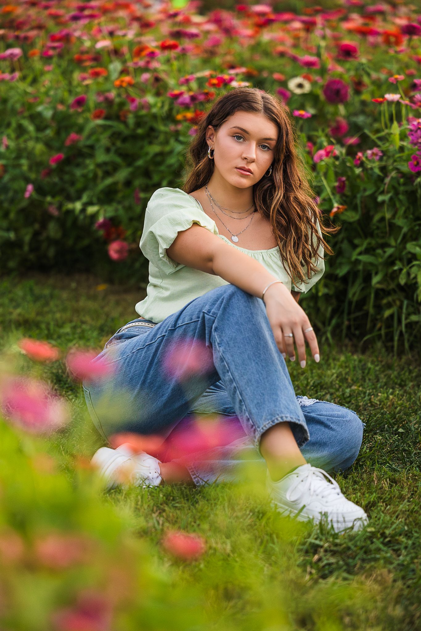 Young woman in green top and jeans sitting in colorful flower garden.
