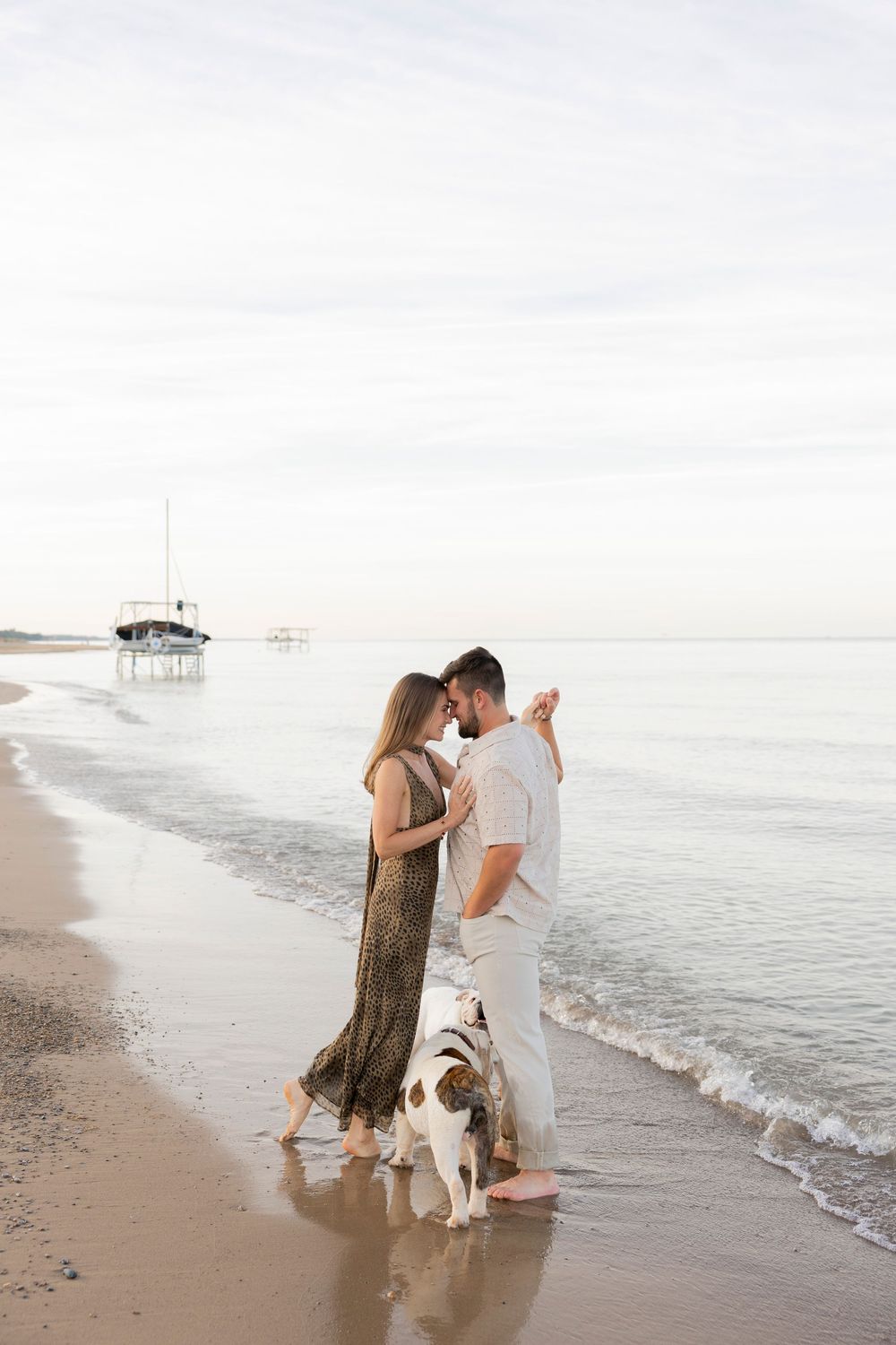 A couple dance together while their dogs are by their feet on a misty beach shoreline with gentle waves rolling in michigan
