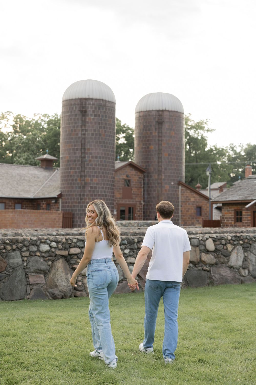 Family walking away together on a grassy lawn with stone wall and brick silos in the background.