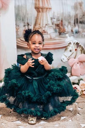 Smiling toddler girl in a green tulle dress holding a treat, posed in front of a carousel backdrop.