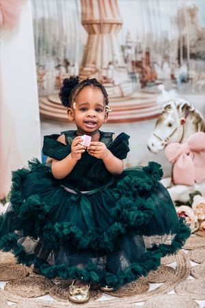 Toddler girl in a dark green tulle dress smiling at a carousel-themed birthday photoshoot.