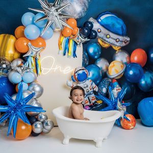 Festive balloon garland with blue and orange balloons arranged with silver stars decorates birthday bathtub photoshoot scene.