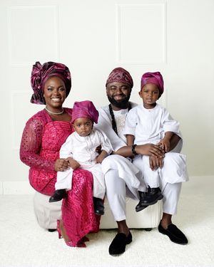 A joyful Nigerian family in vibrant traditional attire poses for a portrait, wearing pink and white outfits with matching headwear.
