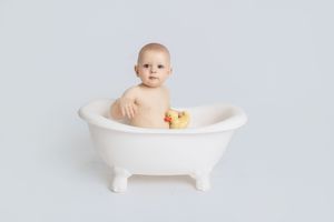 Baby splashing and playing in a classic white freestanding bathtub filled with water.
