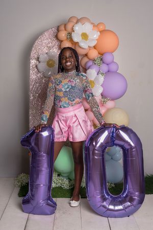 Purple number balloons spelling 10 with pink and colorful party decorations including floral garlands and pastel balloon arch.