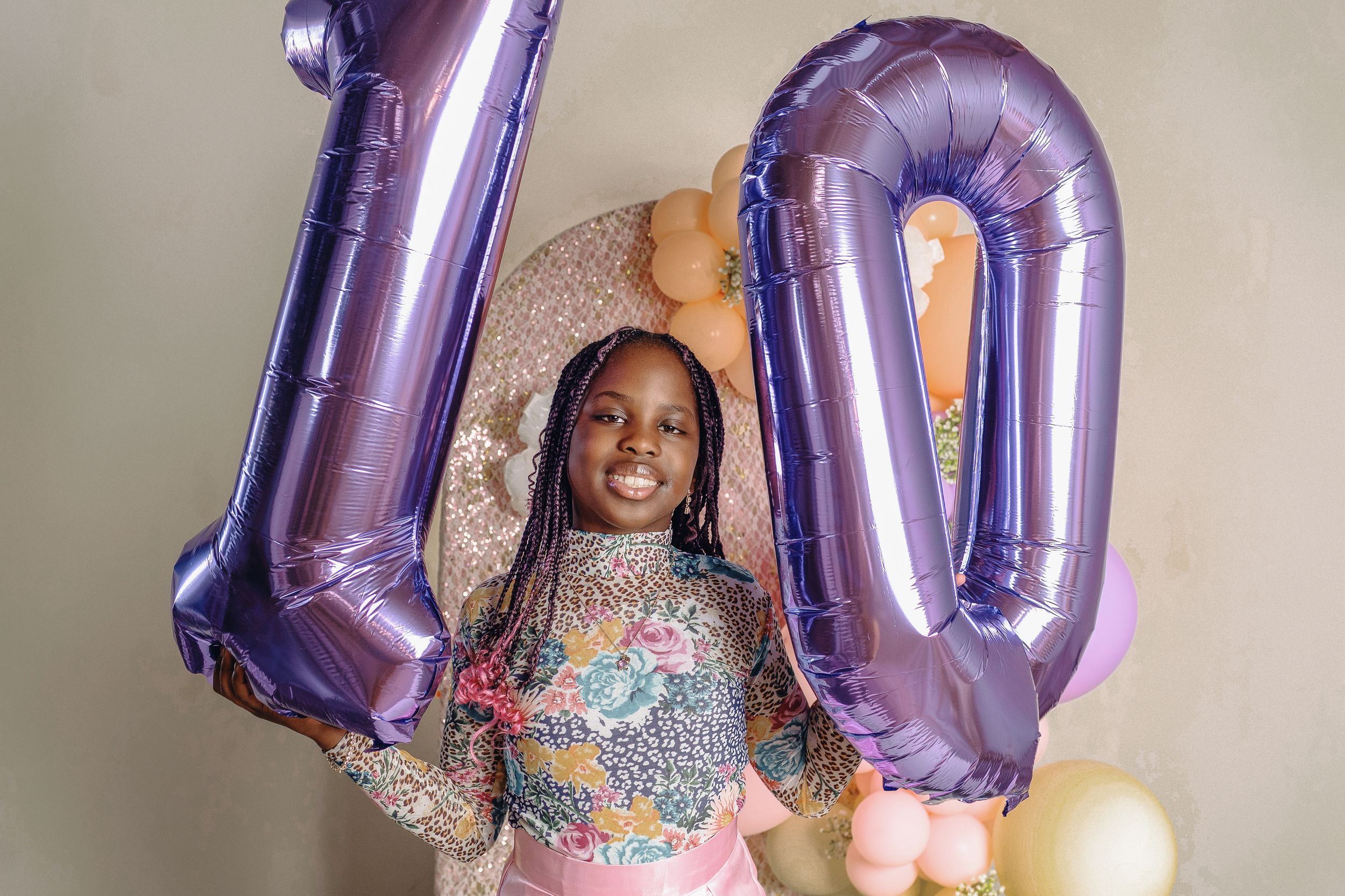 Purple metallic number 10 balloons float beside someone wearing a sparkly multicolored dress at a celebration.