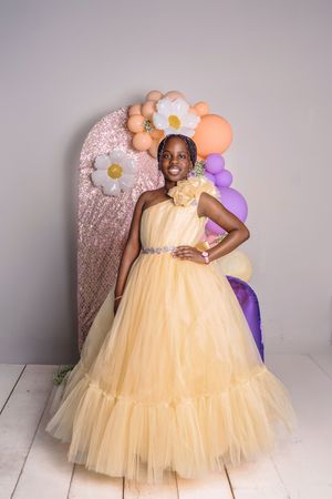 Beautiful ballgown with a yellow tulle skirt and floral decorative backdrop captured in studio portrait setting.