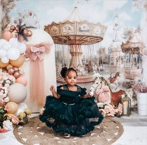Young girl in dark green tulle dress poses at carousel-themed birthday party with balloons and floral decorations.