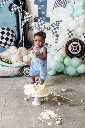 Baby's first birthday cake smash with racing theme, balloons, and checkered flags decorations.