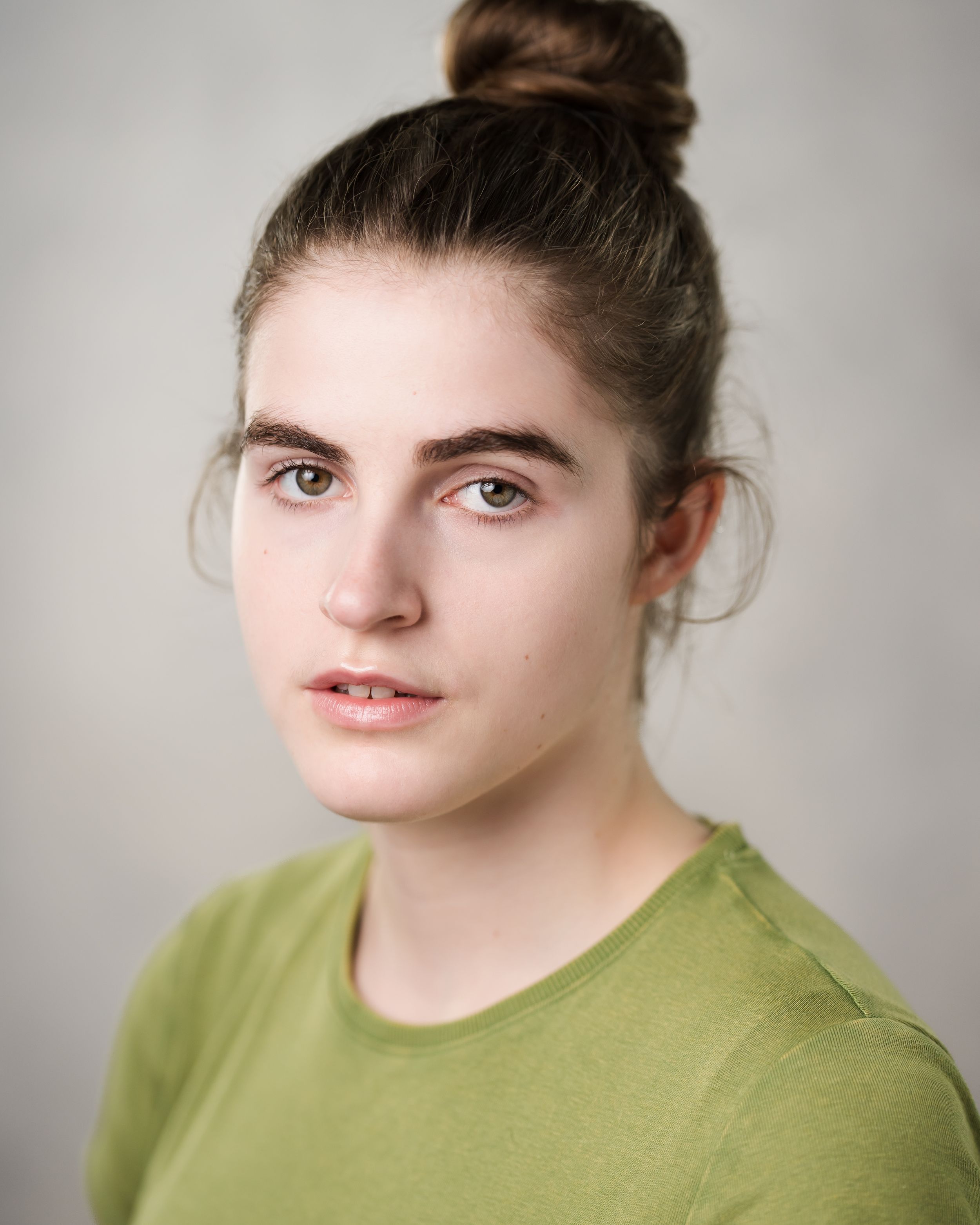Professional headshot of person in green shirt with hair in bun against neutral background. Headshots in Guildford, Surrey.