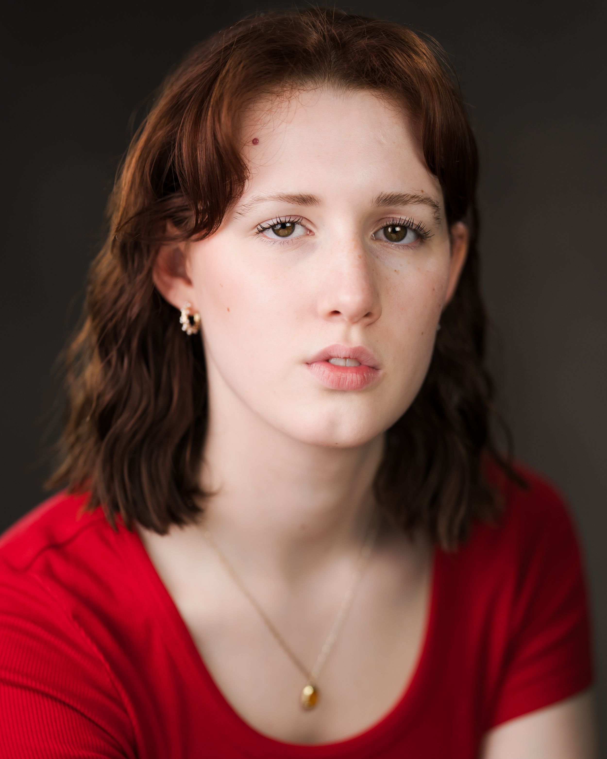 Professional portrait of person wearing red sweater with shoulder-length hair against dark background. Headshots in Guildford, Surrey.