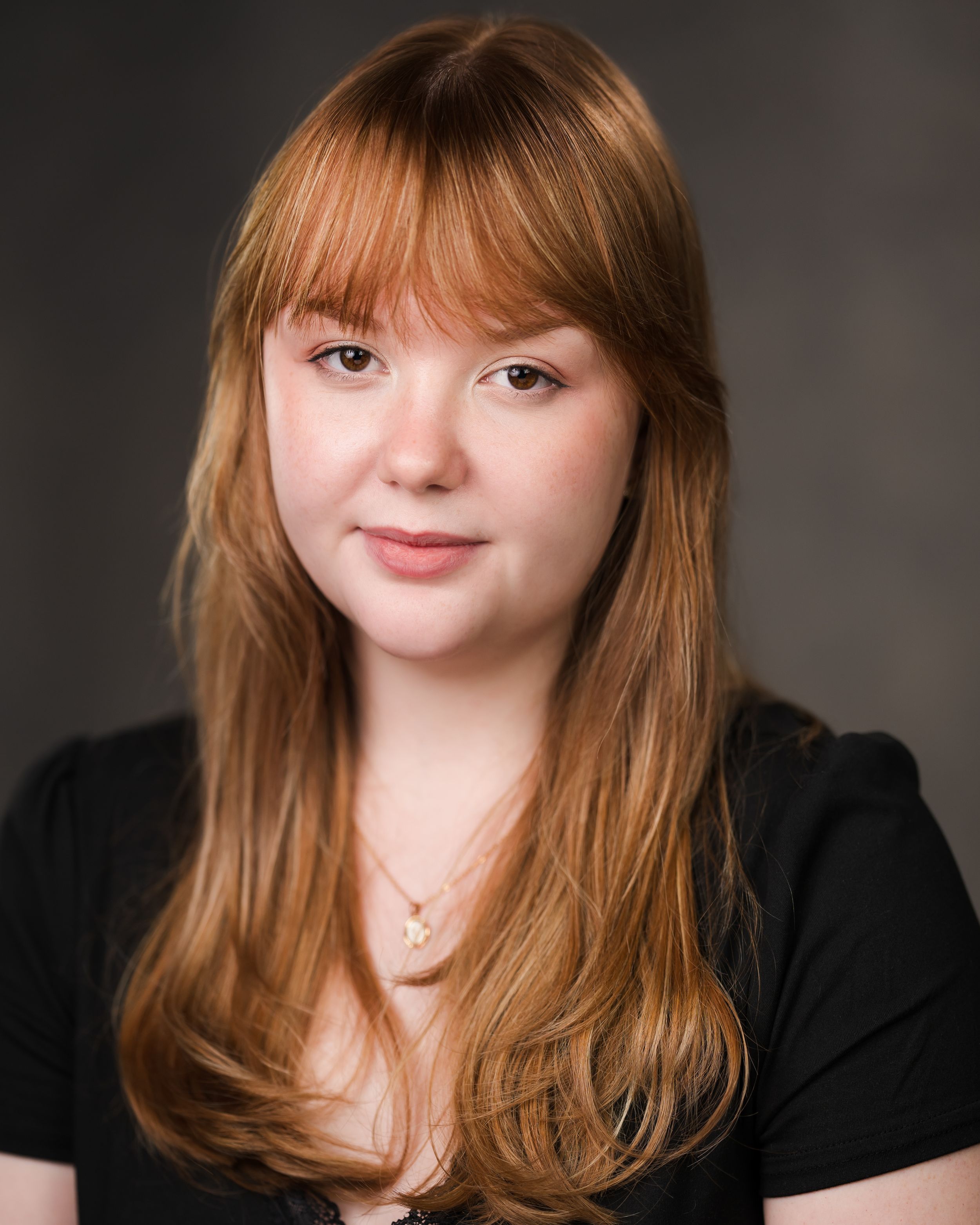 Professional portrait of person with long hair wearing black top against dark background. Headshots in Guildford, Surrey.