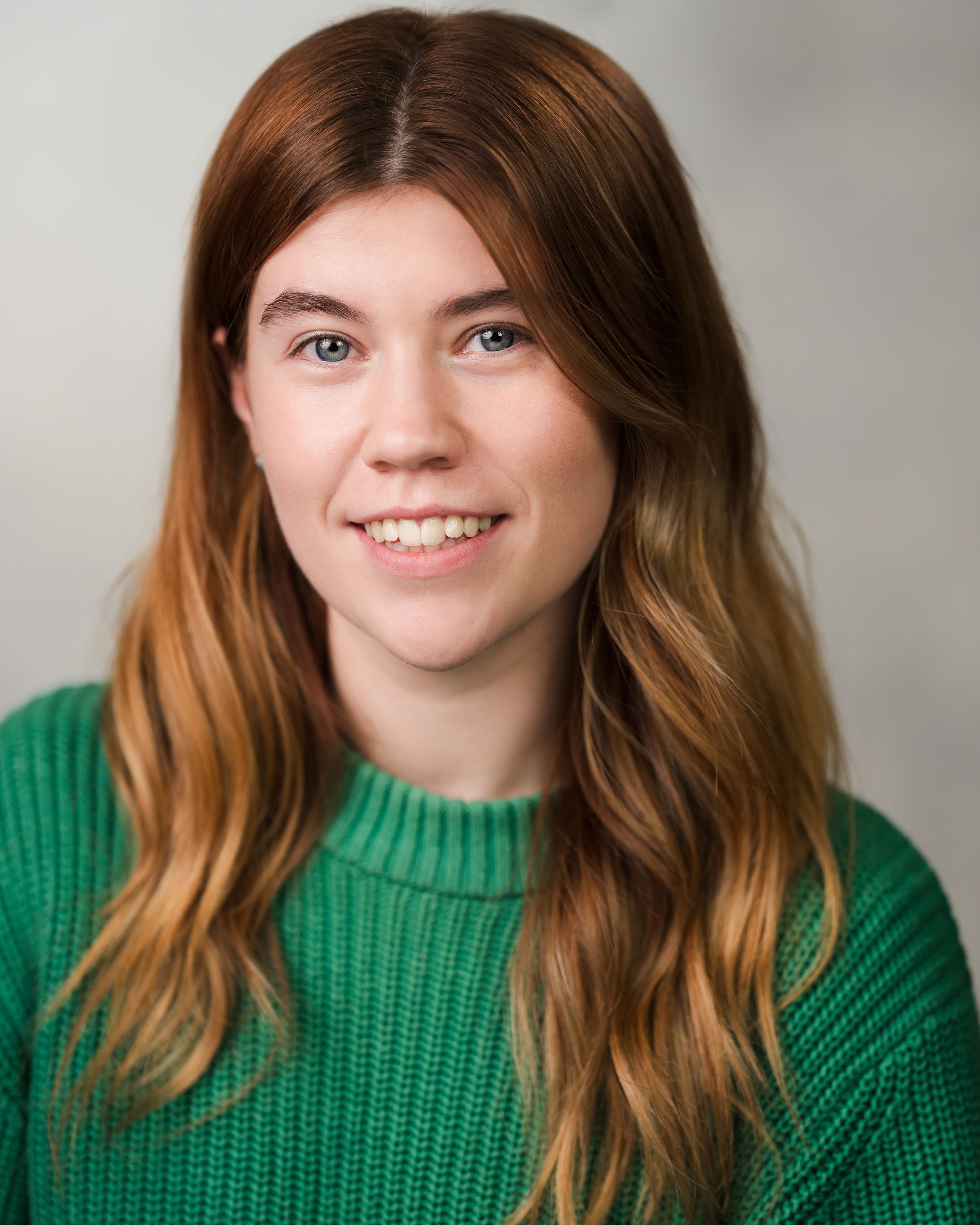 Professional portrait of person in green sweater with wavy hair against neutral background. Headshots in Guildford, Surrey.