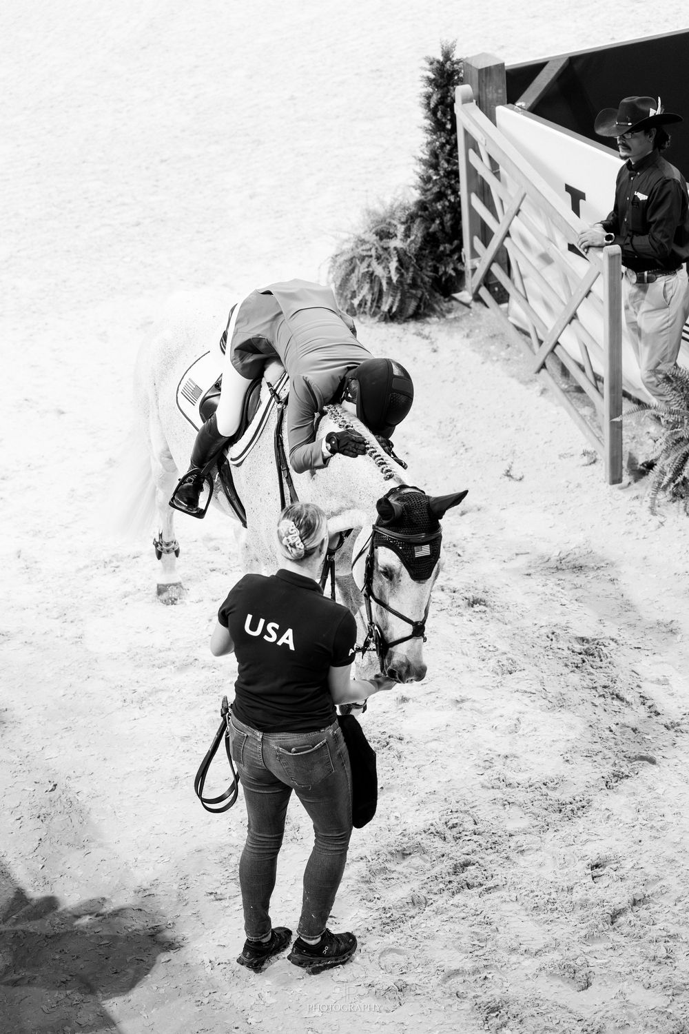 Black and white photo of USA team member holding a white horse with rider at an equestrian competition.