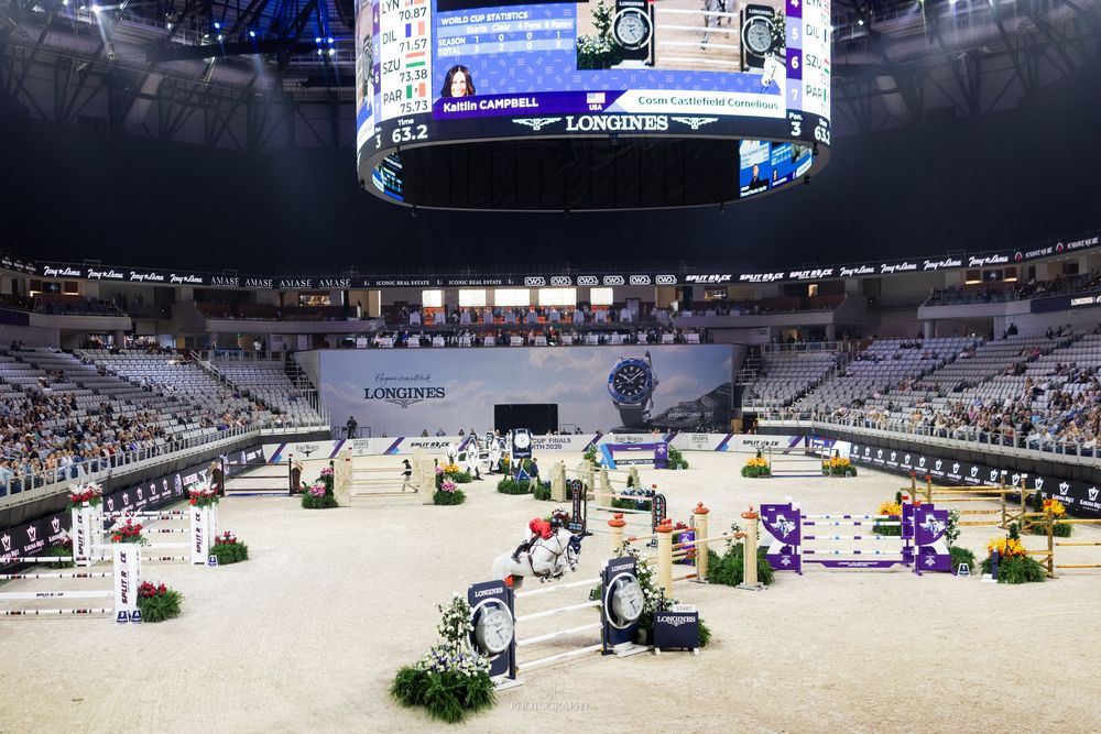 Indoor equestrian show jumping competition at a grand arena with colorful obstacles and Longines sponsorship branding.