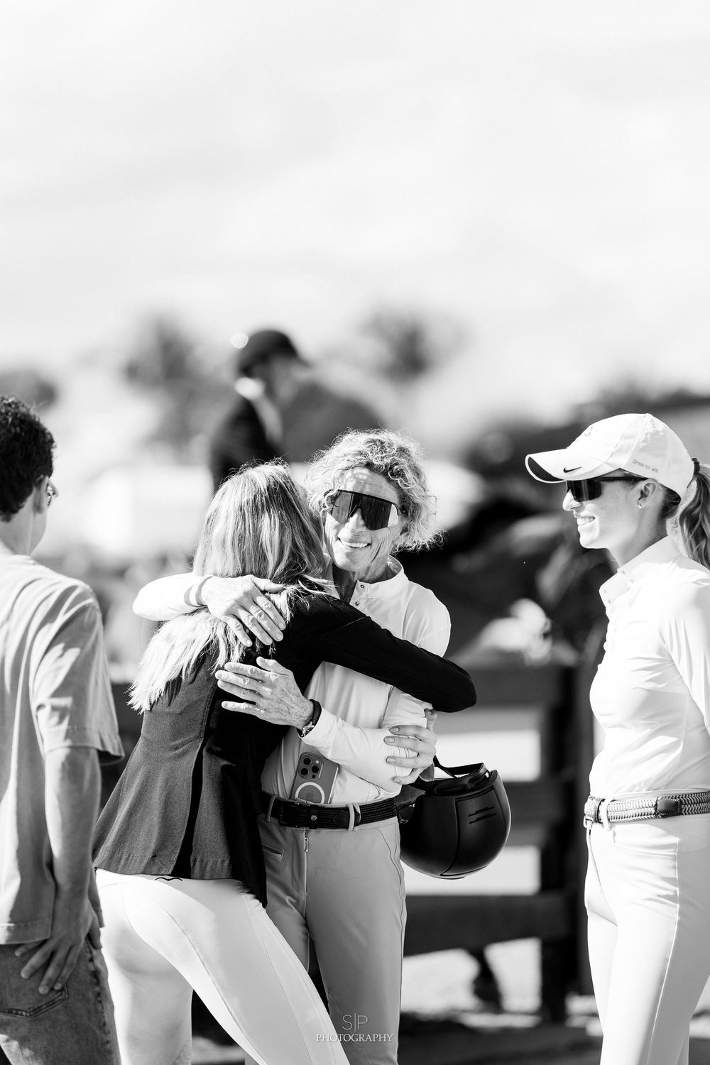 A group of people in white uniforms embrace in a celebratory huddle on a sports field.