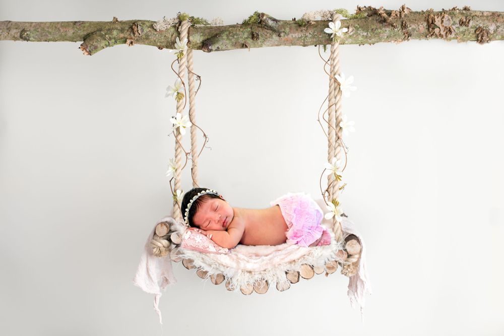 Rustic wooden swing setup with pink accents for newborn photography.