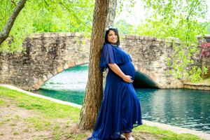 Person in flowing blue dress poses near stone wall beside tranquil pond.