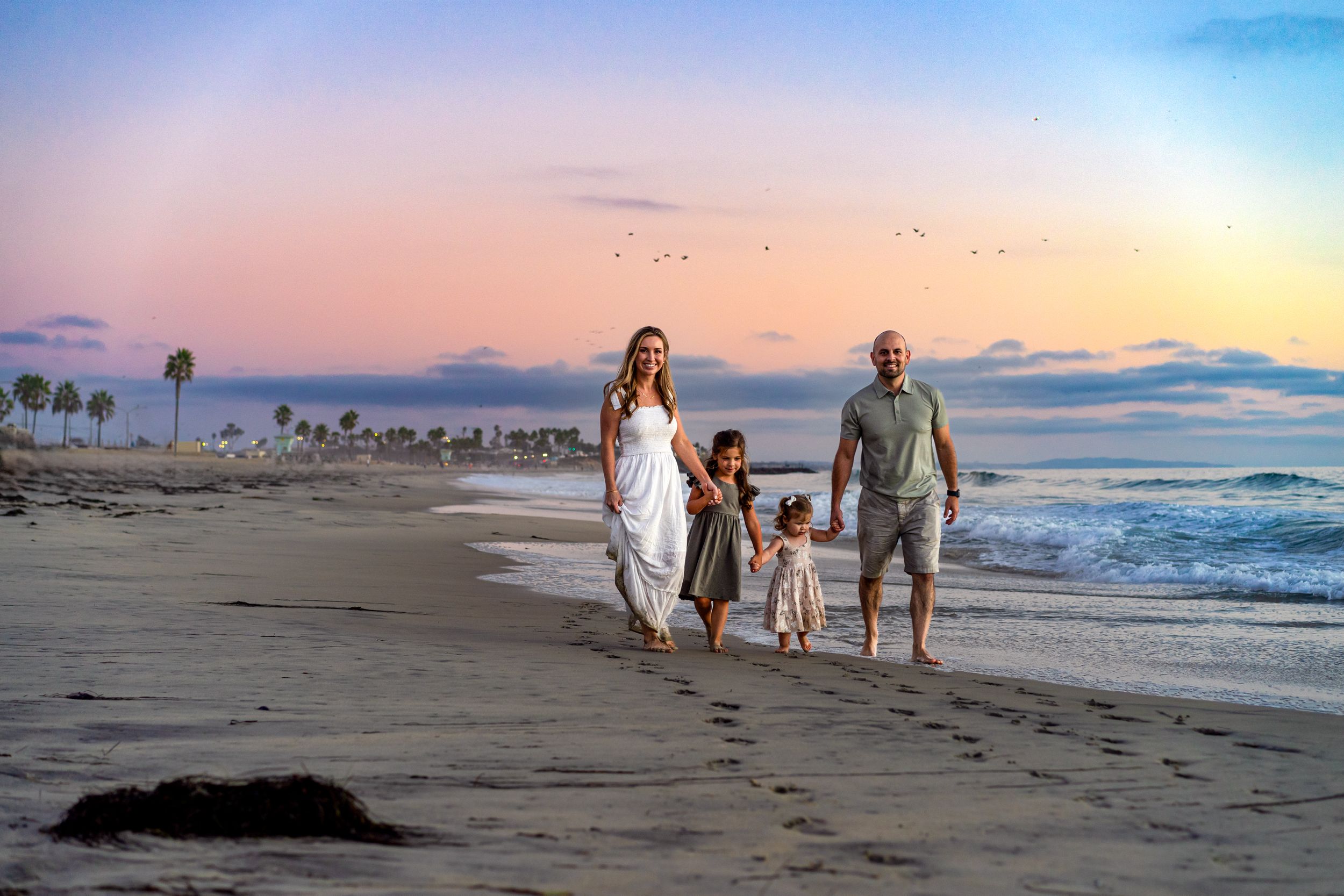Peaceful beach scene at sunset with people walking along the shoreline.