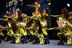 Dancers in shimmering gold costumes perform a synchronized dance routine on stage during a theatrical performance.