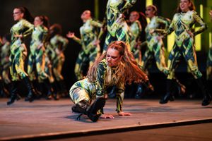 Dancers in green costumes perform energetic choreography during a stage production.