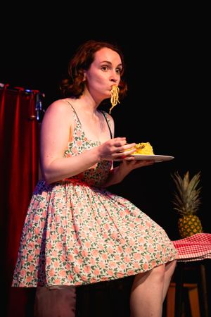 Theatrical performance featuring vintage-style floral dress and pineapple prop on stage. Theatre photography in Surrey.