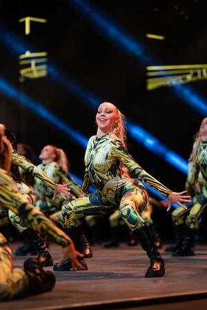 Dancers in camouflage costumes perform dynamic choreography with dramatic blue stage lighting.