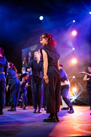 Dancers in black costumes perform on a dimly lit stage with dramatic blue and purple lighting effects.