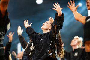 Graduates in black caps and gowns raise their hands in celebration during an outdoor graduation ceremony.