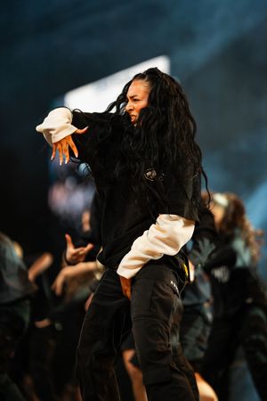 A dancer in black performs an expressive contemporary dance movement sequence against a dark background.