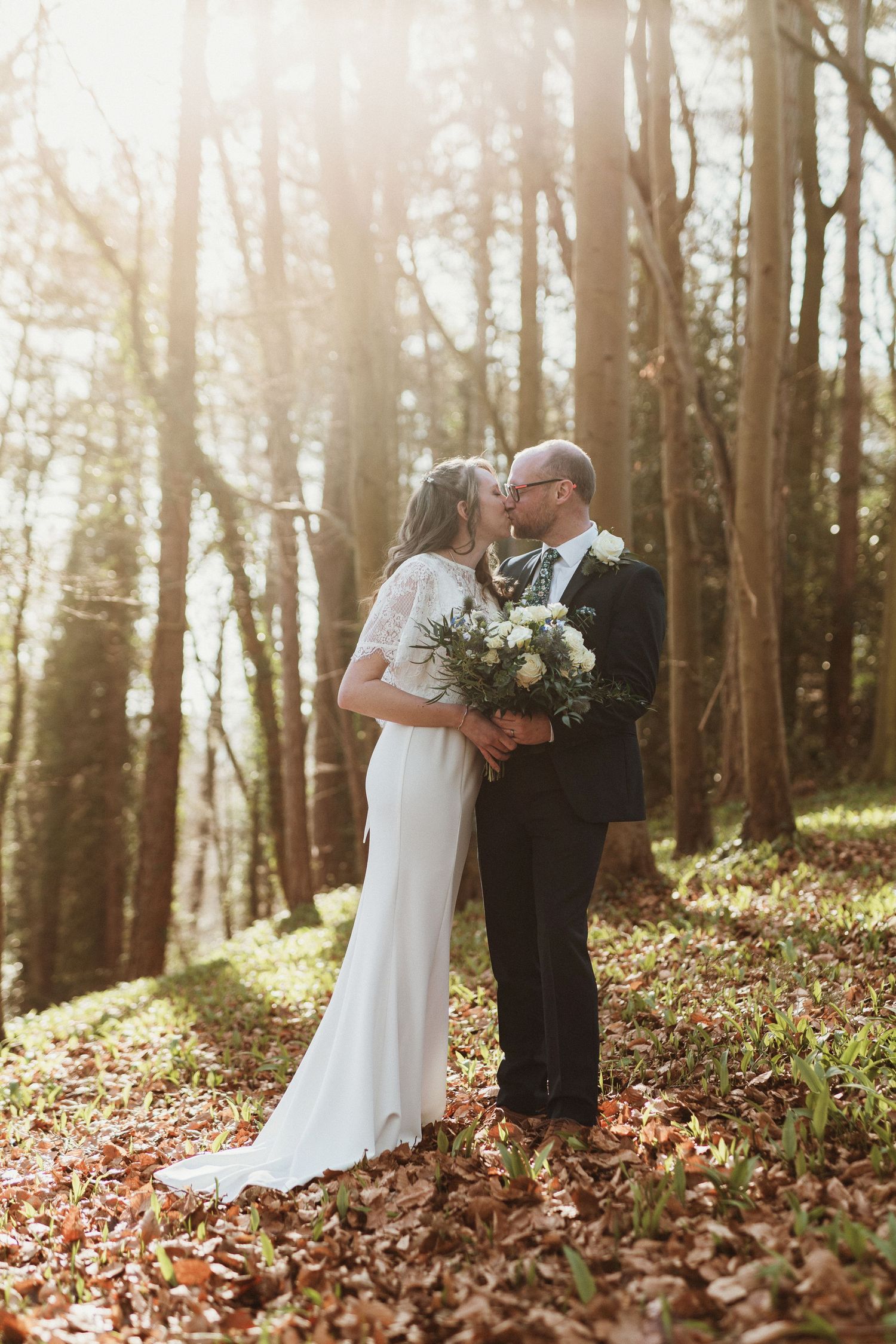 Romantic woodland wedding portrait with sunlight filtering through trees.