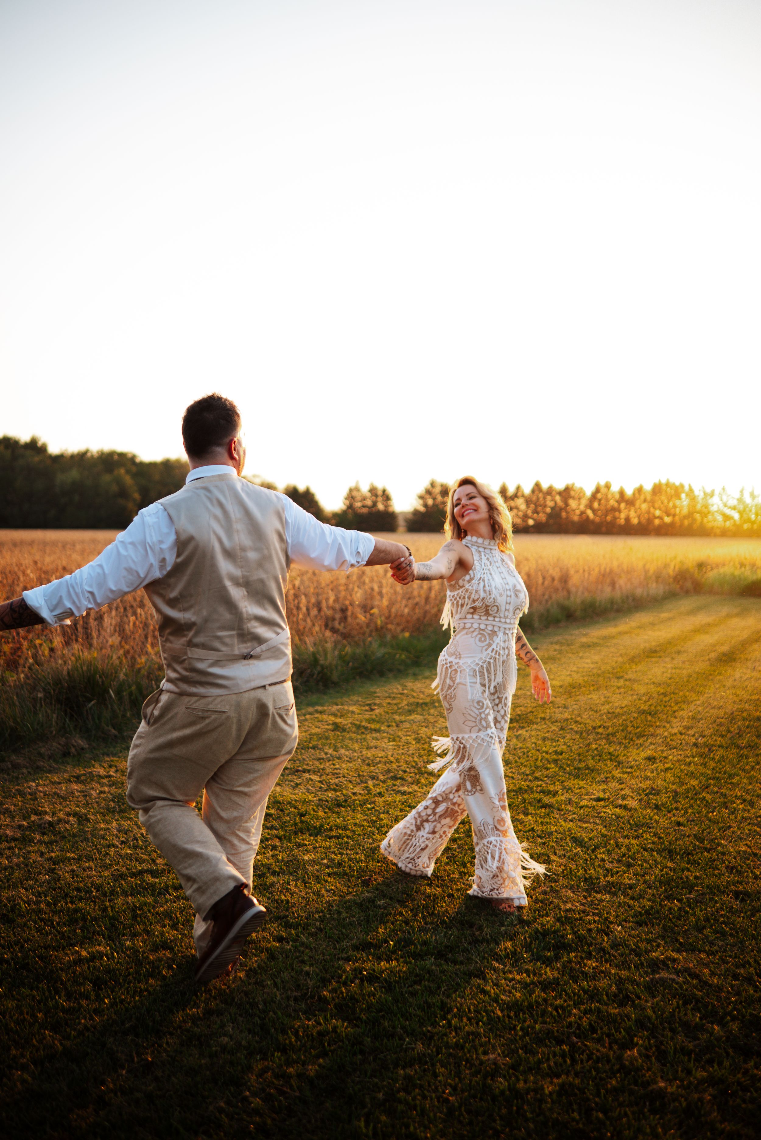 A couple dances playfully in a golden sunlit field at sunset creating a romantic and joyful moment.