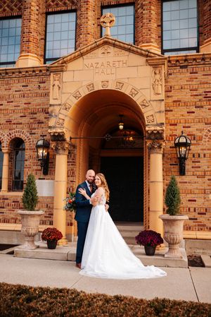 A couple poses in formal attire outside historic Nazareth Hall, a brick building with ornate architectural details and lanterns.