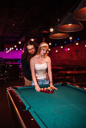 A couple plays pool together at a dimly lit bar and overhead lamps illuminating the green felt table at Howards in Bowling Green, Ohio.