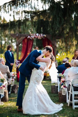 A romantic wedding couple shares a dramatic dip kiss pose during their outdoor forest ceremony.