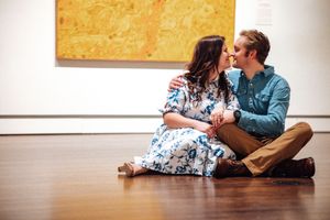 A couple sits together on a hardwood floor in casual attire, sharing an intimate conversation.