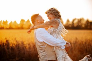 Couple embraces in golden wheat field at sunset during romantic photoshoot.