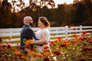 A couple sits together in a garden filled with vibrant red and orange flowers during golden hour sunset at the Stables.