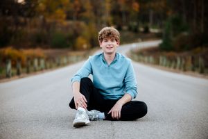 A series of outdoor portraits taken on an empty autumn road showing someone in a light blue shirt sitting and posing.