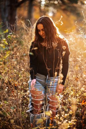 Person in ripped jeans sits among wildflowers in golden sunlight creating a dreamy autumn outdoor scene.